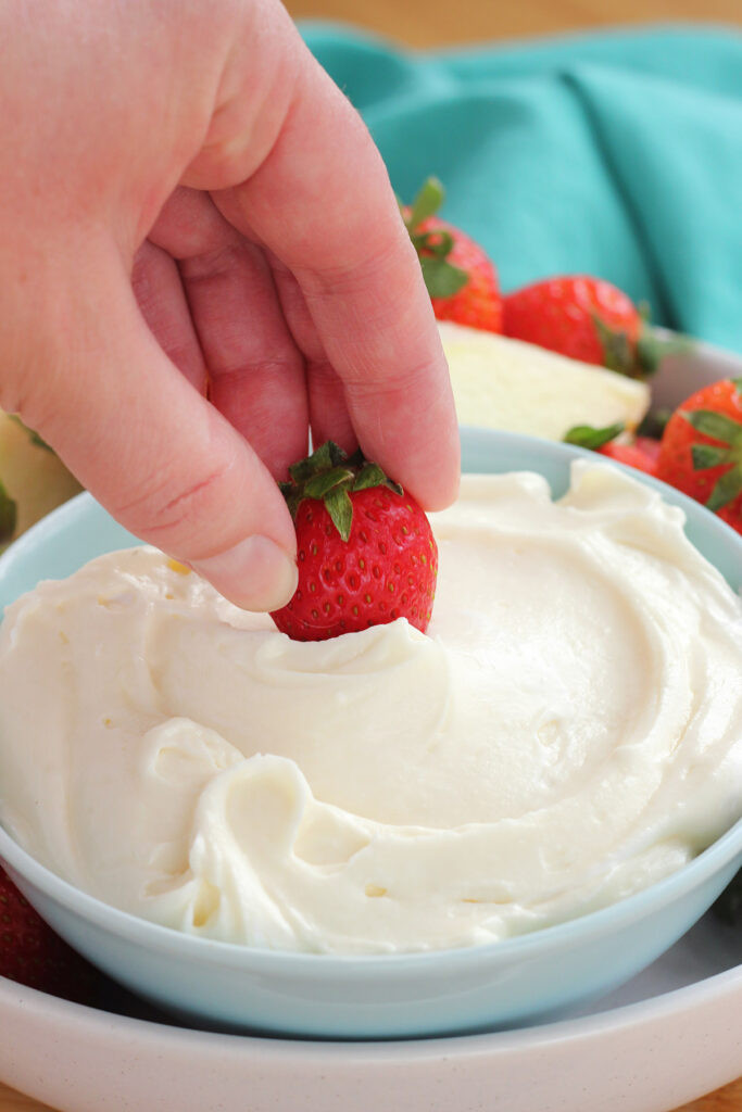 blue bowl filled with white cream cheese dip with a single strawberry being scooped into the center.