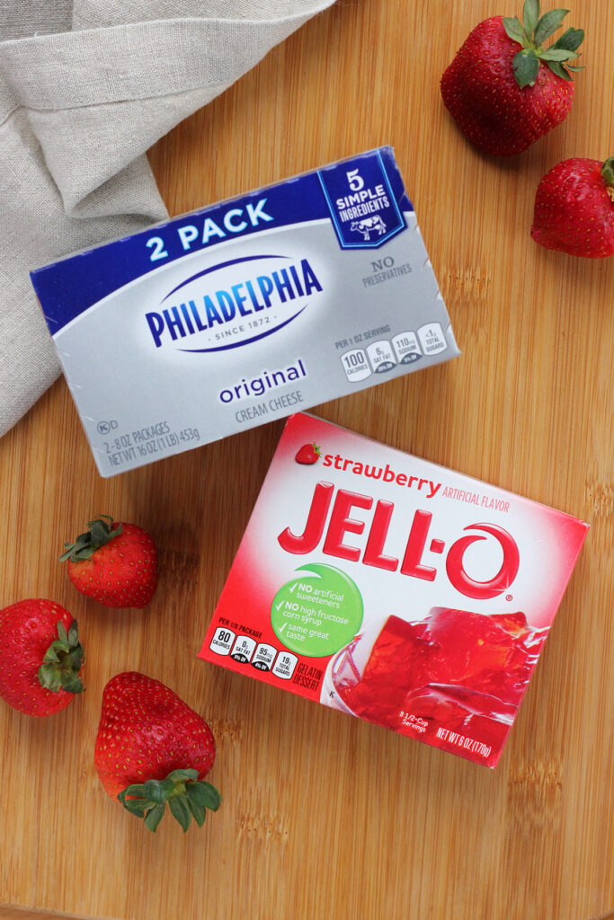 2 pack box of Philadelphia cream cheese along with a box of strawberry Jello sitting on a wooden cutting board with a tan napkin and fresh berries