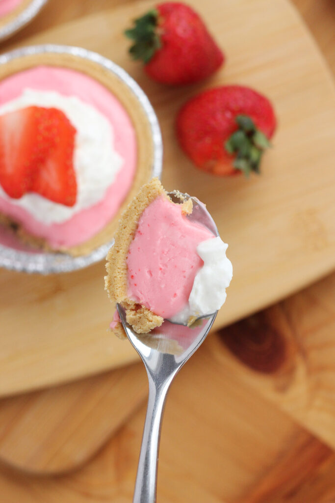 bite of strawberry cheesecake on a spoon hovering over the top of a mini cheesecake