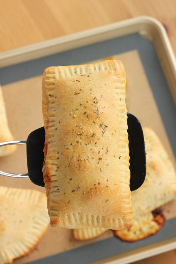 golden brown pizza pocket being held over the baking tray on top of a black spatula