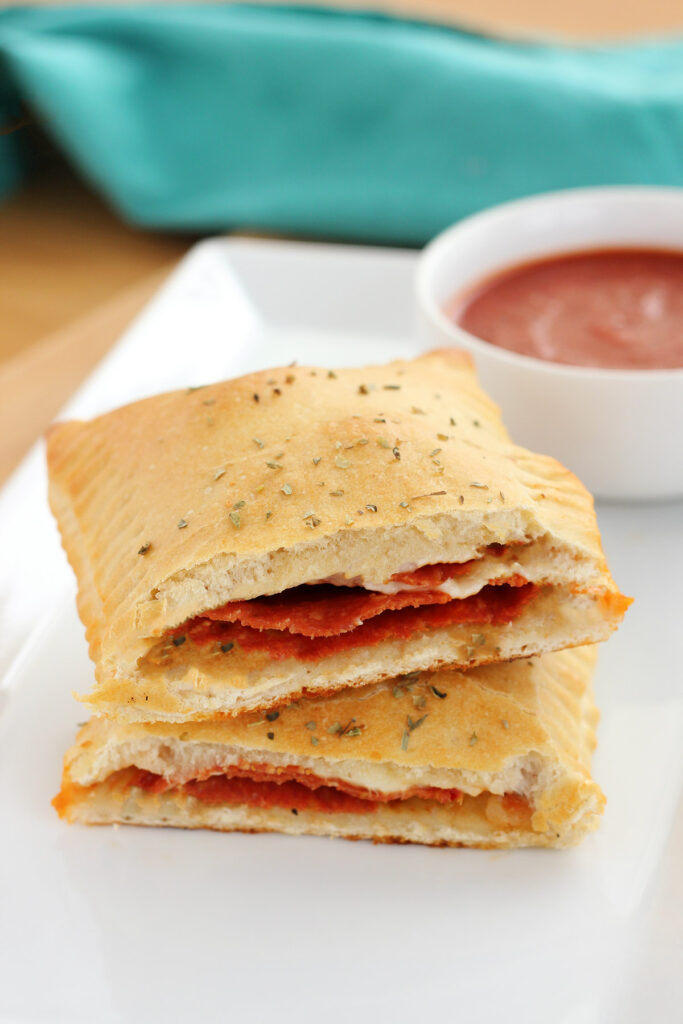 single hot pocket cut in half sitting on a white plate with a side of marinara in a small white bowl