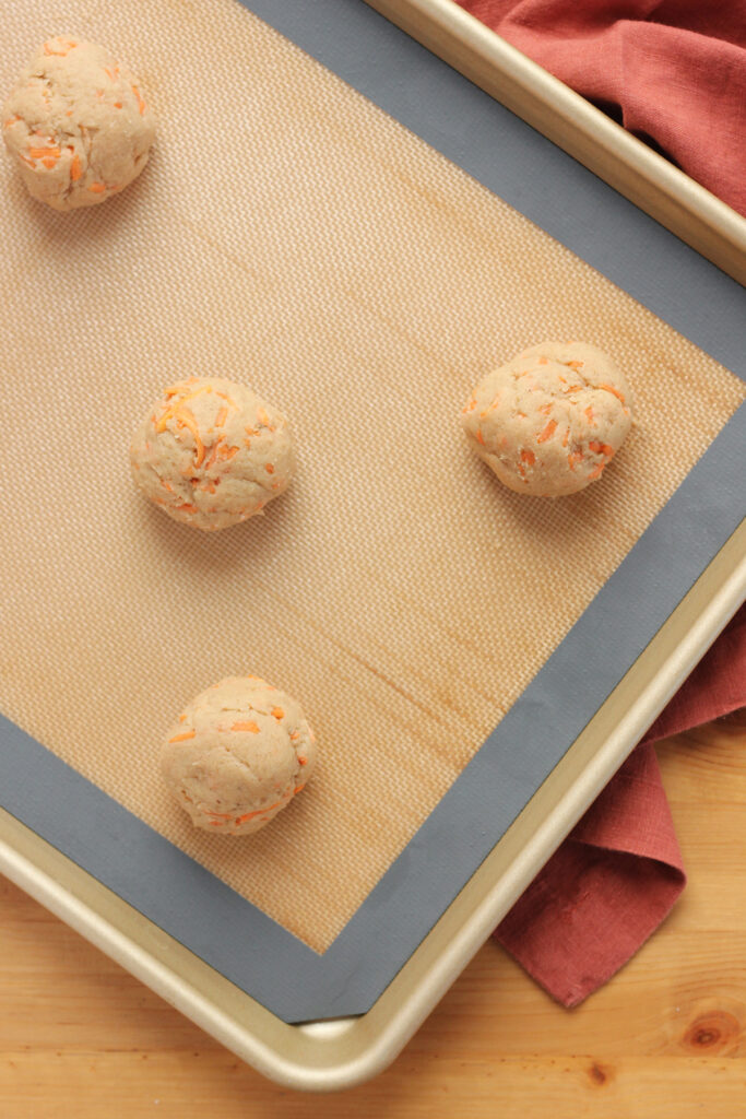 carrot cookie dough balls rolled and placed on a baking tray that has been lined with a silicone spatula. 
