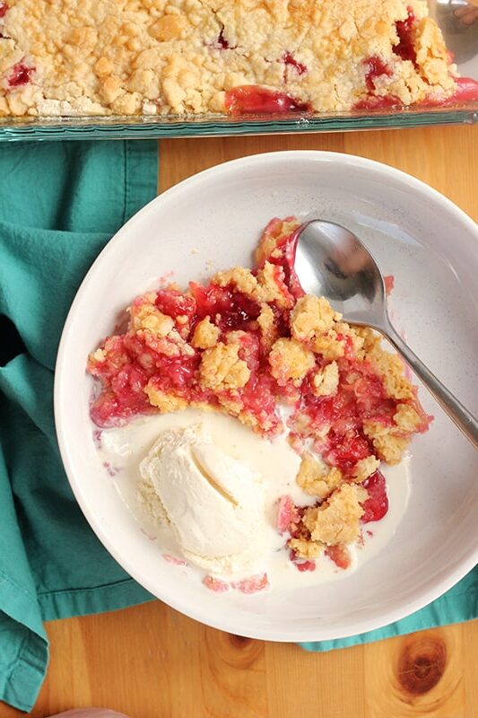 wide white bowl filled with cherry cobbler and a scoop of melting ice cream. A spoon is sitting off to the side