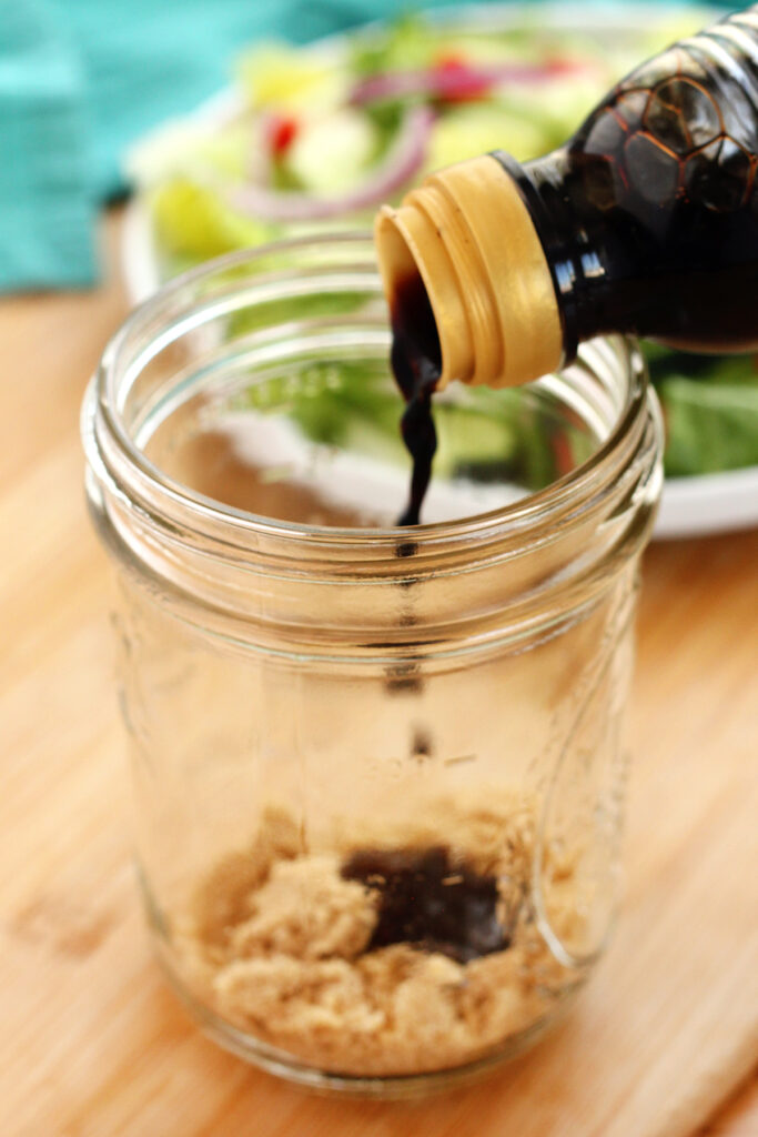 balsamic vinegar being poured into a mason jar with brown sugar sitting on the bottom