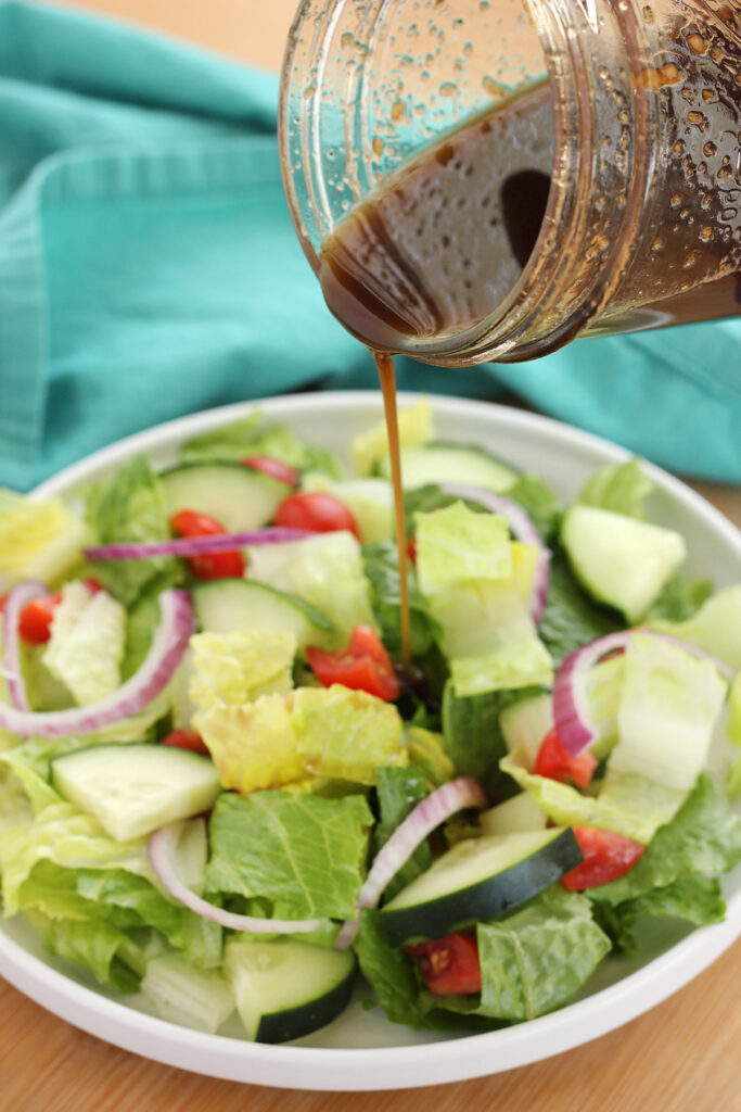 balsamic vinaigrette being poured out of a mason jar onto a side salad