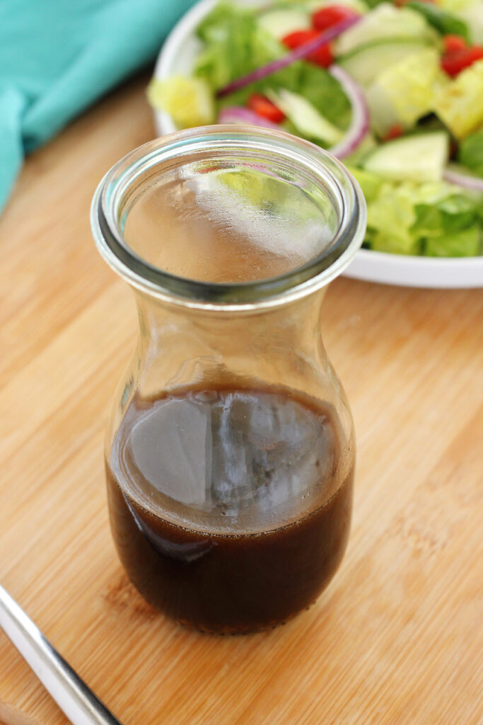 jar filled with dressing sitting on a wooden tabletop with a salad in the background