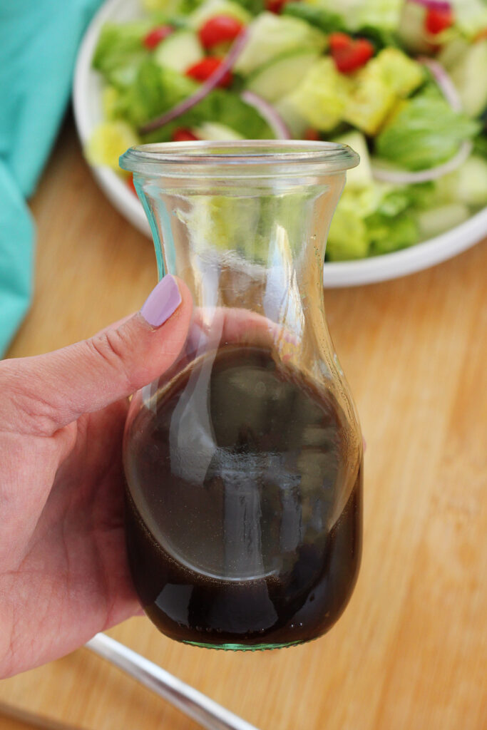 hand holding a jar filled with salad dressing over a wooden cutting board and a side salad