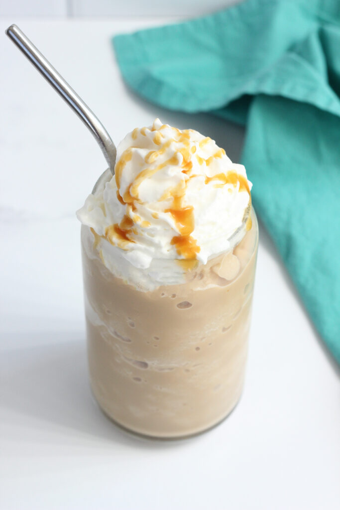 glass filled with frozen coffee that is topped with whipped cream and caramel drizzle with a metal straw