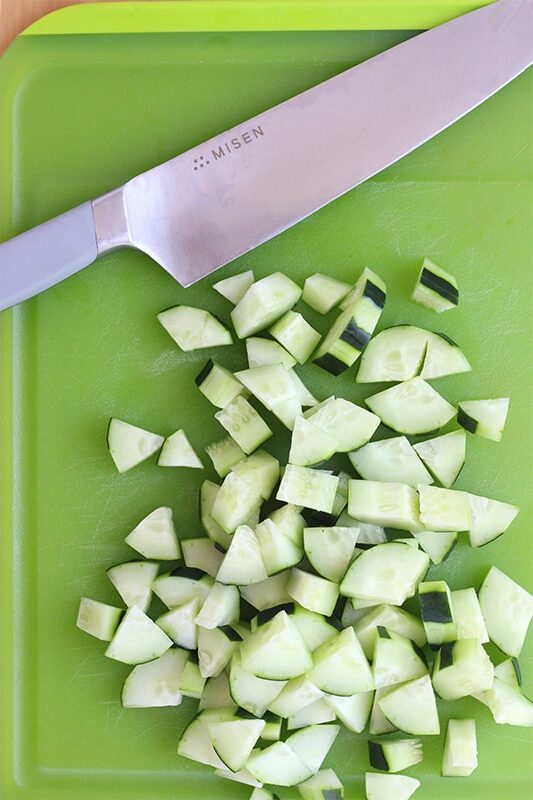 green cutting board with chopped cucumber pieces and a misen chef knife