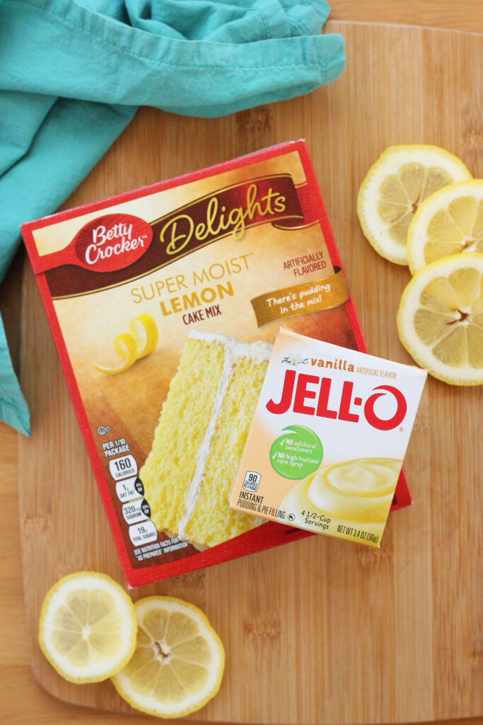Lemon cake mix and a vanilla pudding mix sitting on a wooden cutting board with lemon slices