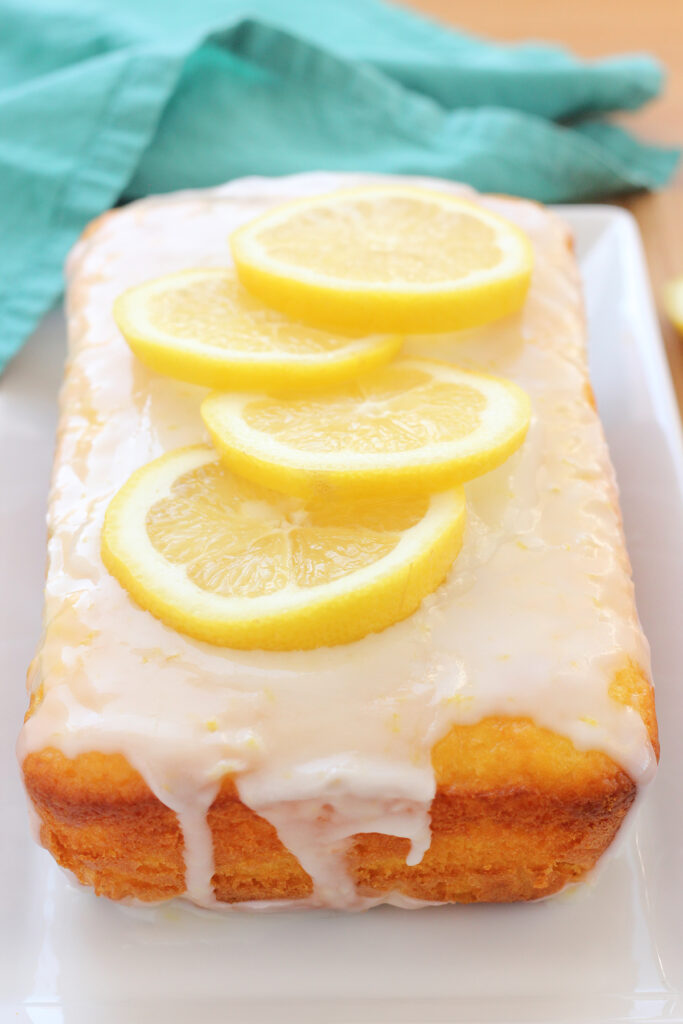 close up image of a lemon cake dripping with glaze and fresh lemon slices