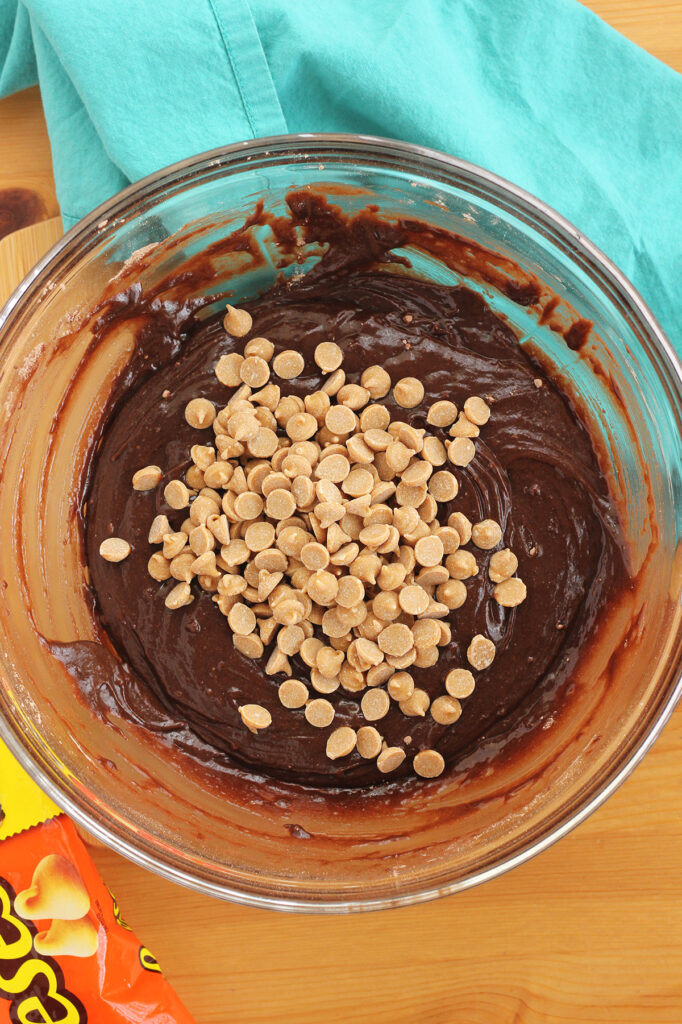 mixing bowl filled with brownie batter and a handful of peanut butter chips sitting directly on top, unmixed.
