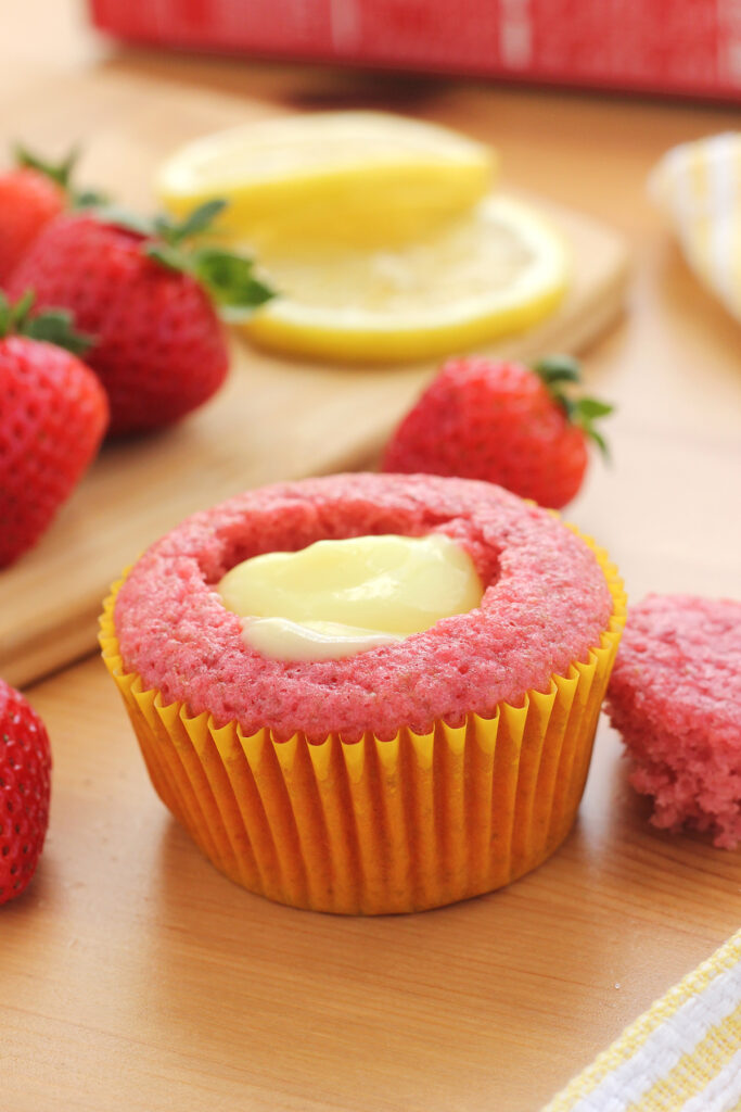 pink cupcake in a yellow cupcake liner with the center cut out and filled with lemon pie filling