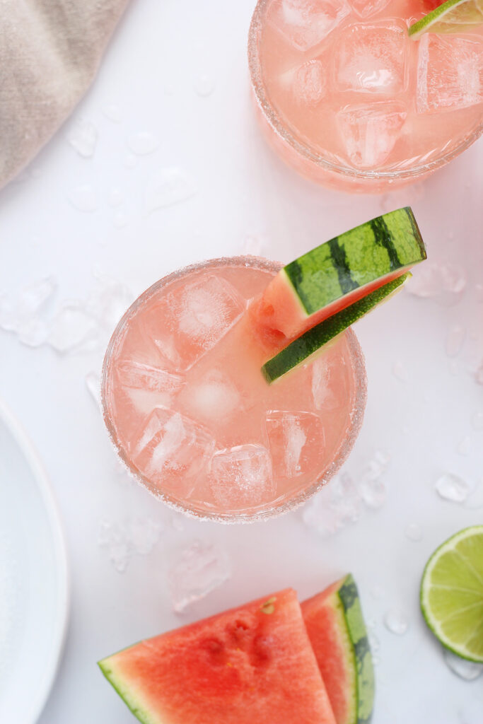 top down image of a watermelon cocktail with ice on a white table top with watermelon wedges and lime slices