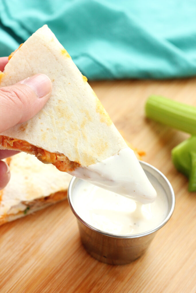 quesadilla triangle being dipped into a container of ranch dressing.