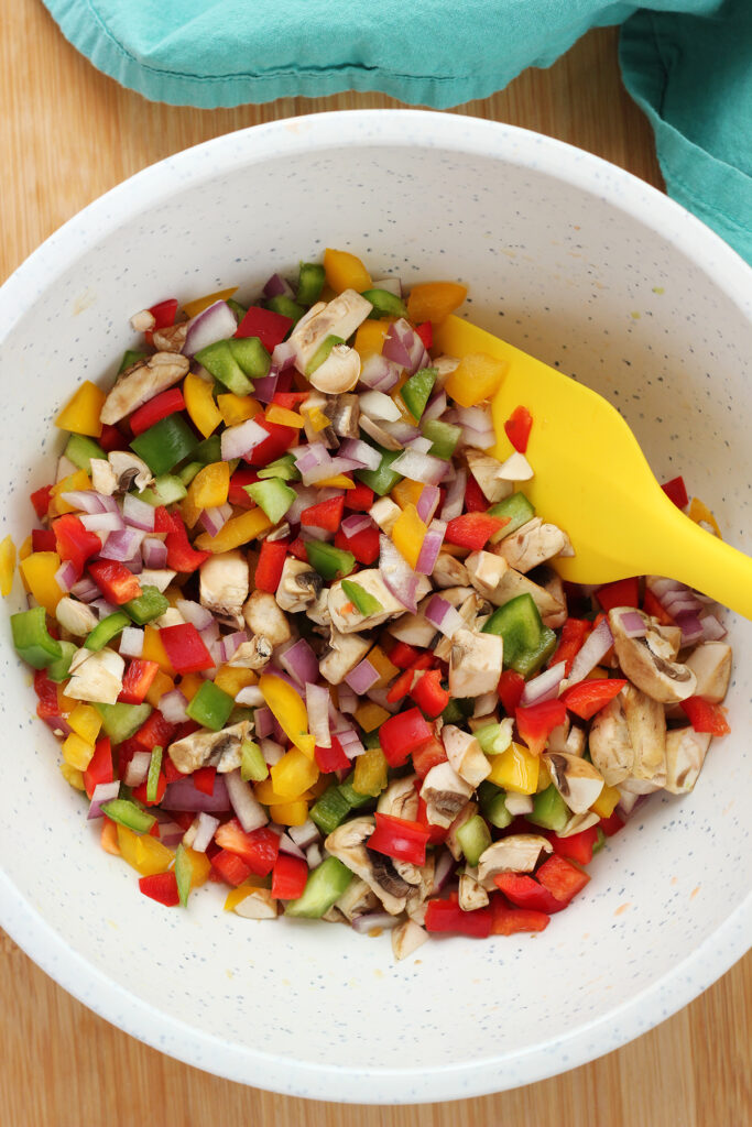 white bowl filled with a variety of colorful chopped vegetables with a yellow silicone spatula sitting inside