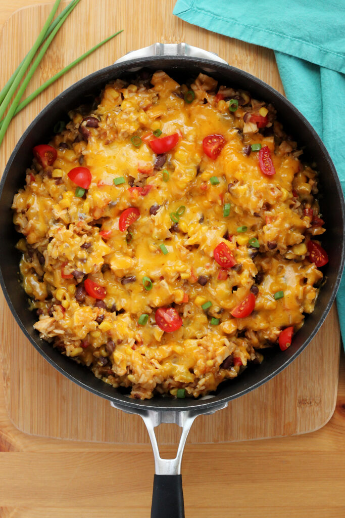 deep black skillet filled with a rice and cheese mixture that is topped with green onion and tomato pieces