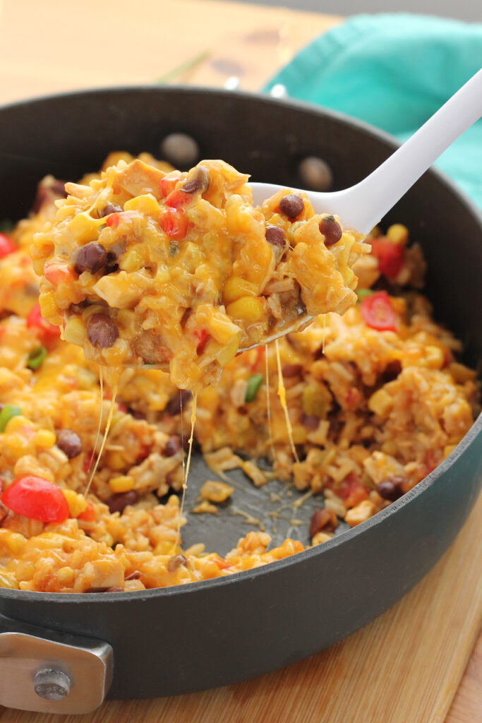 skillet filled with cheesy rice with vegetables with a spoon scooping out a mound