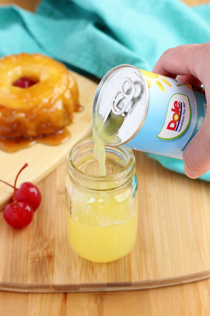 pineapple juice being poured over the top of vodka in a small mason jar shot glass