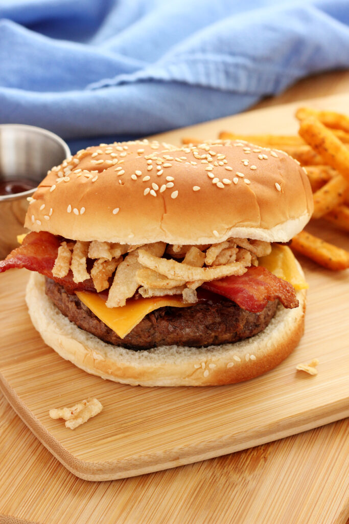 close up image of a burger that is topped with cheese, bacon, and crispy onion rings