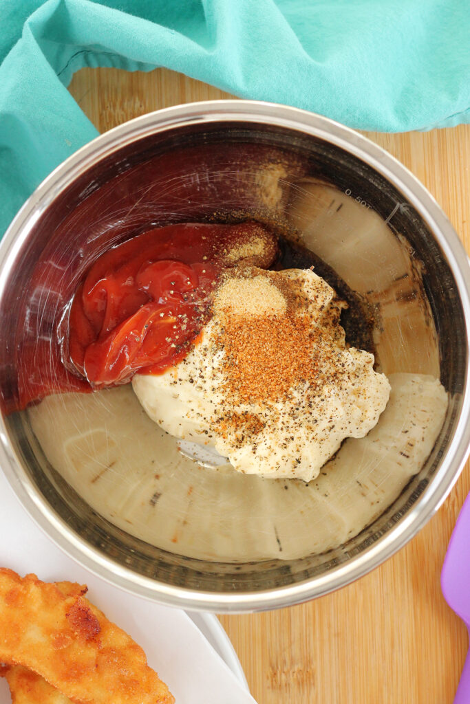 metal mixing bowl that is filled with mayonnaise, ketchup, and seasonings