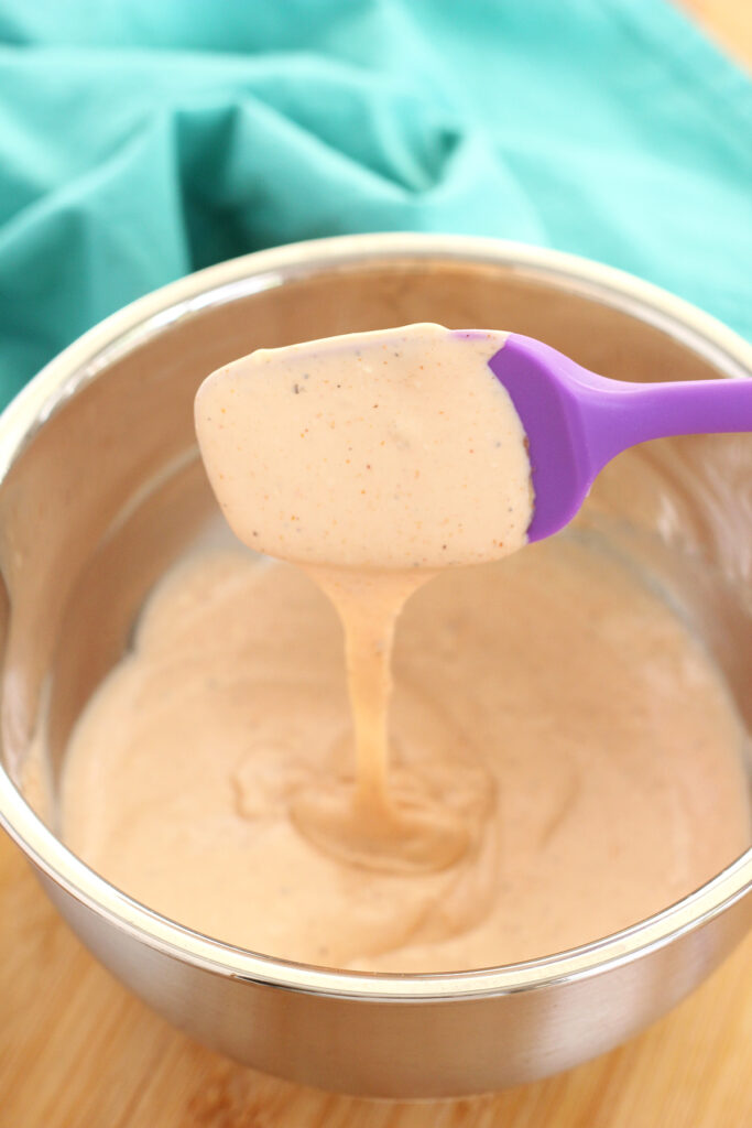 pink dipping sauce in a small metal bowl being stirred with a purple spatula 