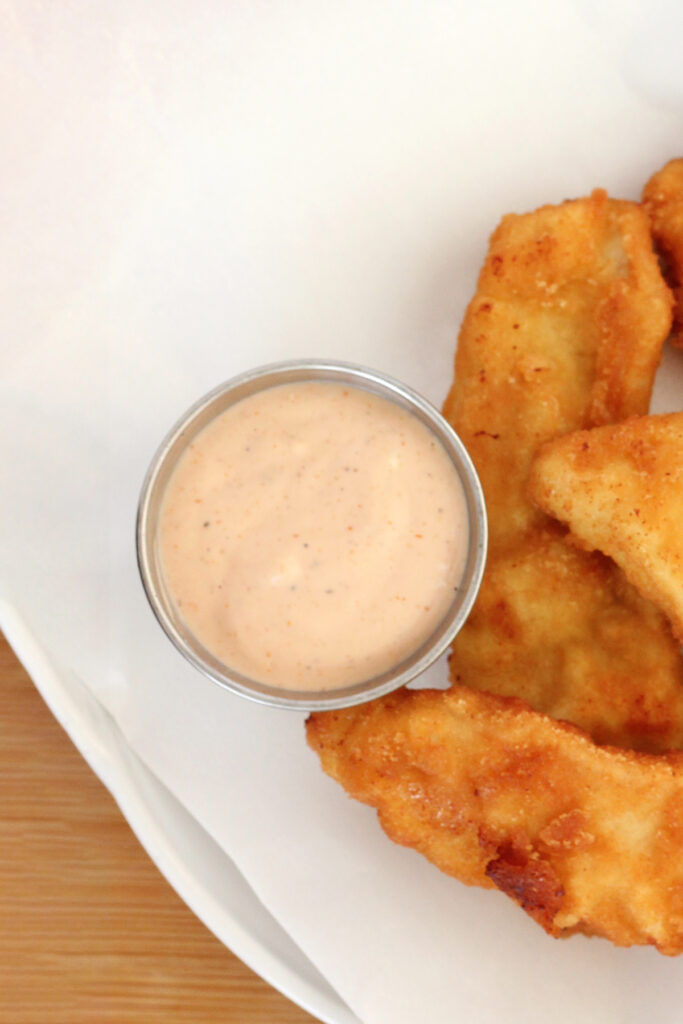 top down image of a small metal dip dish filled with a pink dip with chicken strips off to the side