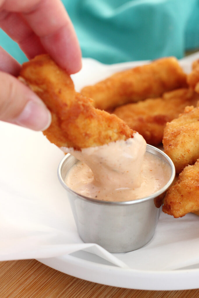chicken finger being dipped into a small metal container that is filled with a pink dipping sauce