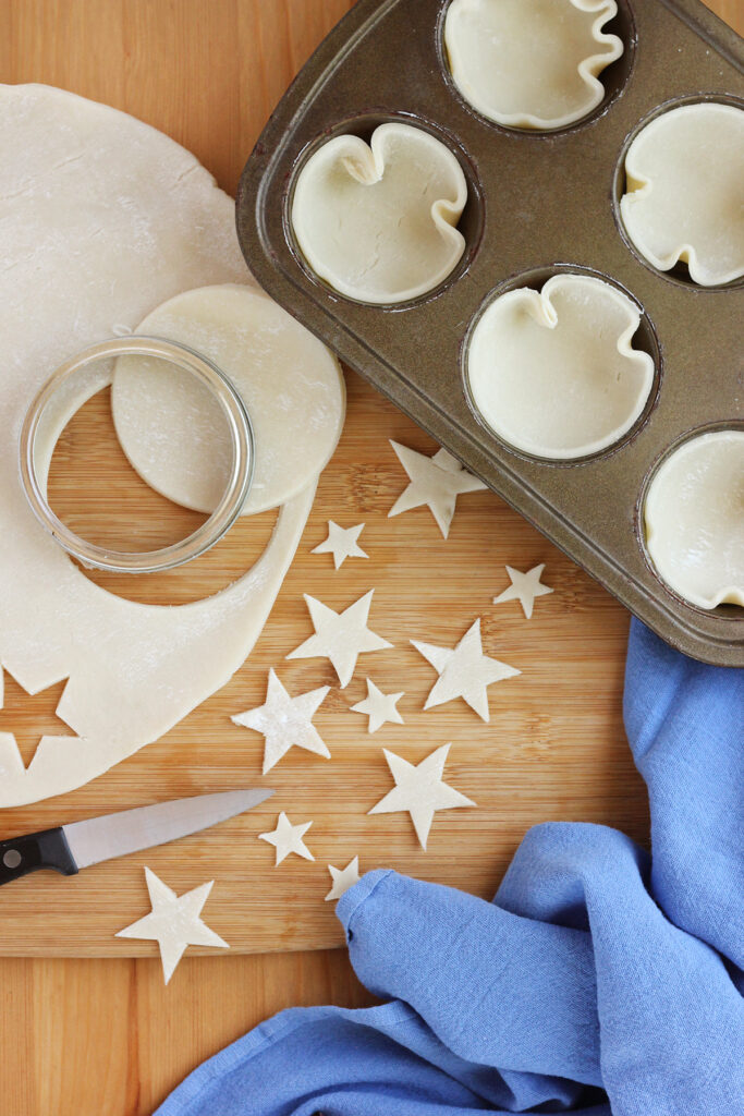 pie crust being cut into star shapes on a wooden cutting board 