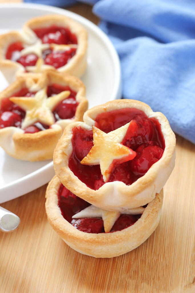 two mini pie cups with star shaped crust stacked onto each other on a wooden cutting board with a blue napkin in the background