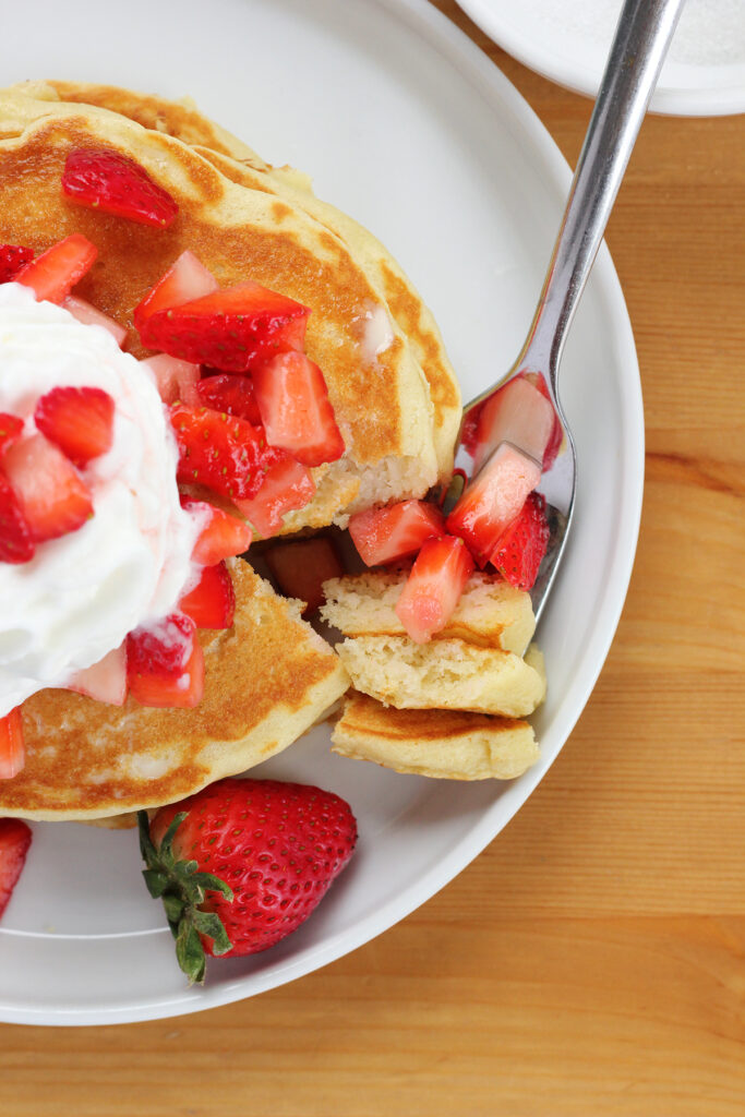 top down image of a white round plate with a stack of pancakes that are topped with chopped berries and whipped cream
