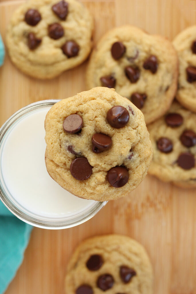 chocolate chip cookie balancing on the edge of a glass of milk