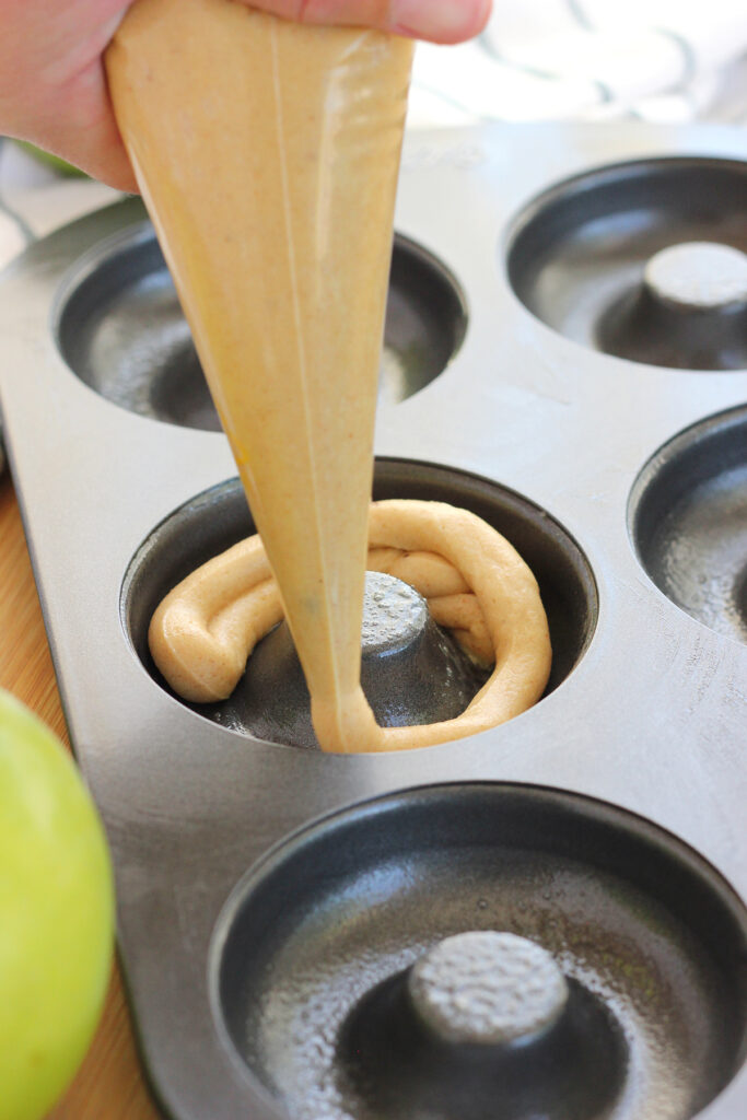 non stick donut pan with donut batter being pipped into one of the round containers