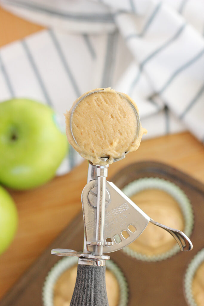 scoop filled with batter hovering over the top of a cupcake tin with unbaked muffins 