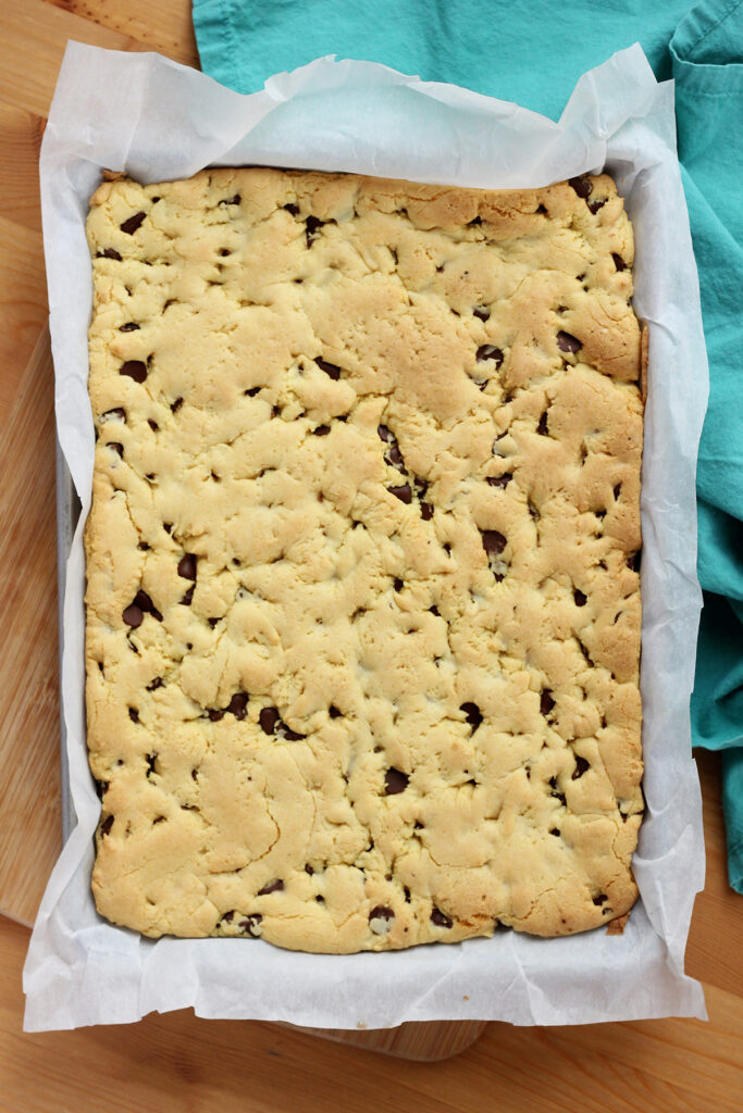 quarter sheet pan that is lined with parchment paper and filled with a giant rectangle baked cookie. A teal napkin is off to the side on the wooden table top