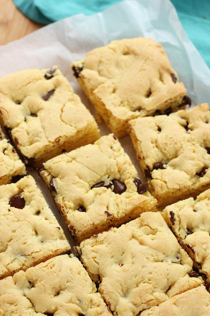 close up image of square cut chocolate chip cookie bars sitting on a white piece of parchment paper
