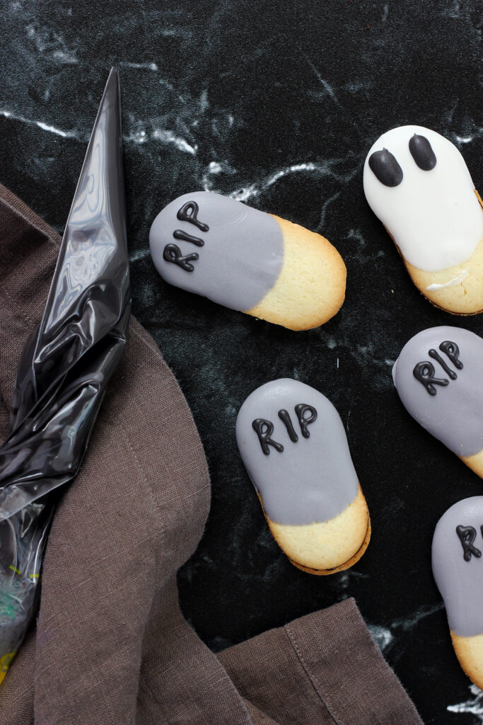close up of milano cookies that have been half dipped in either white chocolate or grey chocolate with RIP written on the grey cookies