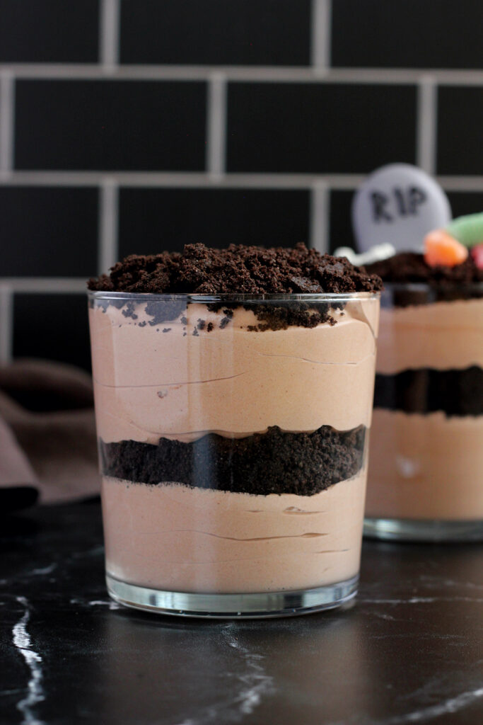 close up of a glass cup that is filled with layers of chocolate pudding and crushed cookies