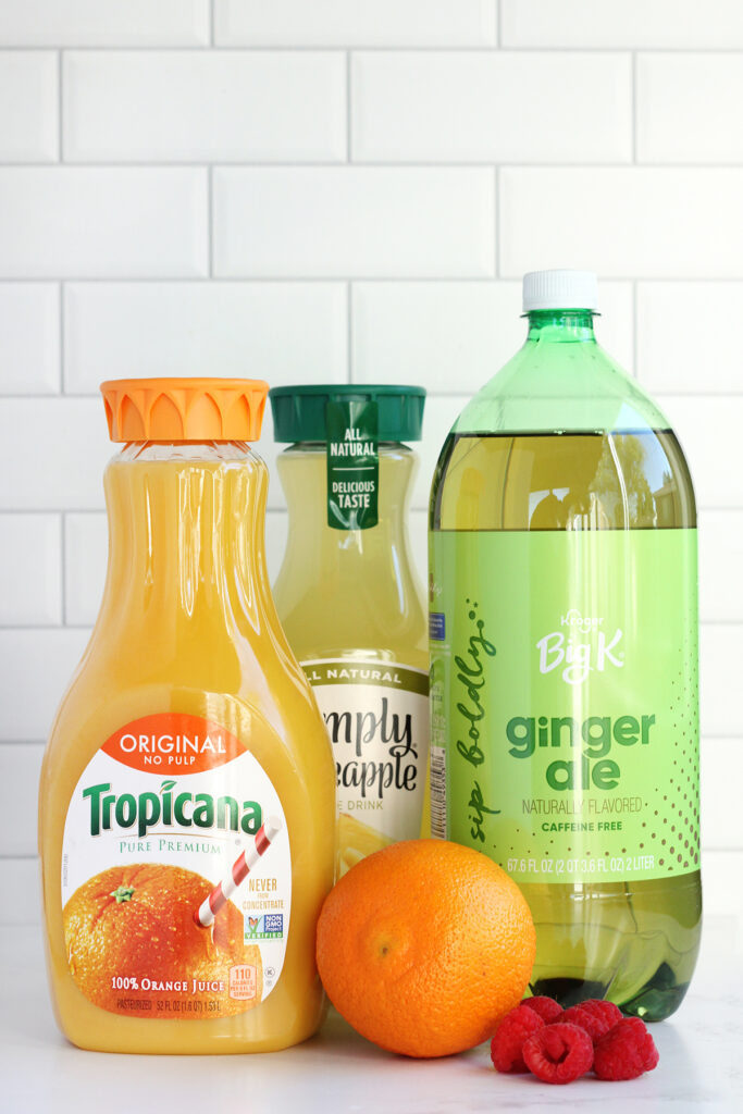 image showing a bottle of tropicana orange juice, a bottle of simply pineapple juice, and a bottle of ginger ale with a fresh orange and a small handful of raspberries on a white coutner top 