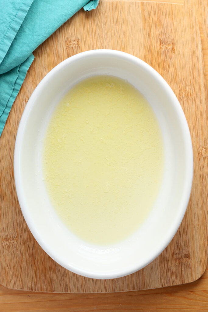 top down image showing a white baking dish that is sitting on a wooden table top with a teal napkin. Inside the dish is melted butter