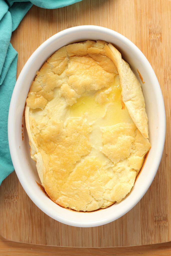 top down image showing a white baking dish that is sitting on a wooden table top with a teal napkin. Inside the dish is a baked pancake that has curled up at the edges