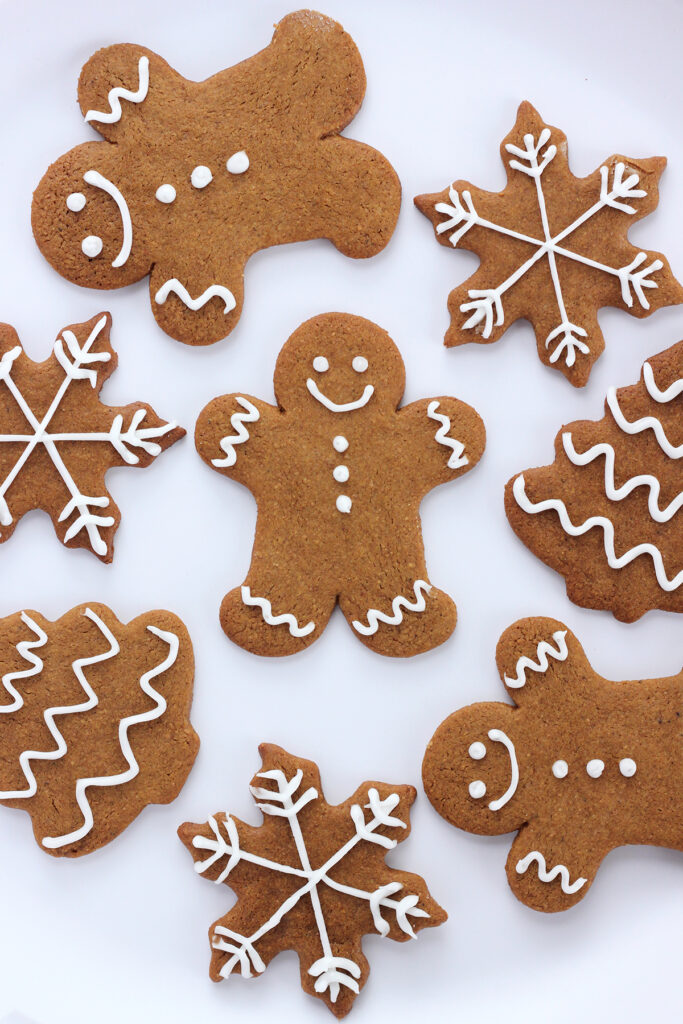 top down shot showing a large white plate layered with holiday shaped gingerbread cookies that have been lightly decorated with a white frosting. Shapes include men, snowflakes, and trees