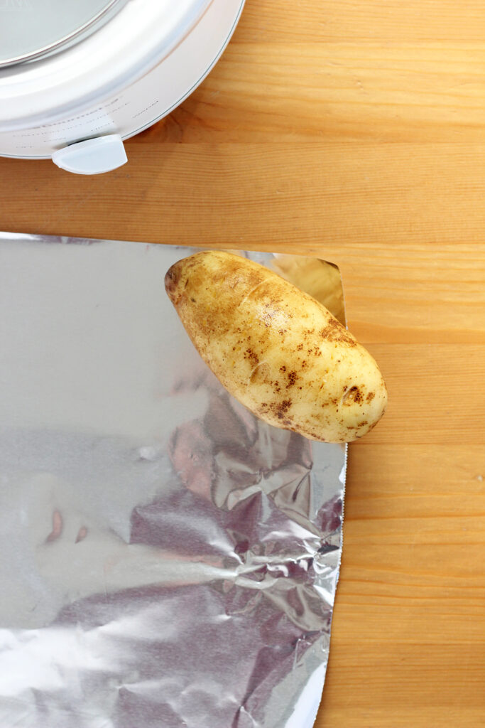 potato sitting in the corner of a sheet of tin foil on a wooden table