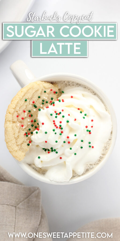 top down image showing a white mug that is filled with coffee, whipped cream, half a sugar cookie, and red and green holiday sprinkles. The mug is sitting on a white table top with a white round plate with more cookies and a tan napkin off to the side. Text overlay reads "starbucks copycat sugar cookie latte"