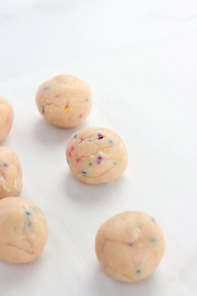 close up image showing undipped truffles that are sitting on a white table top. The truffles have colored sprinkles throughout.