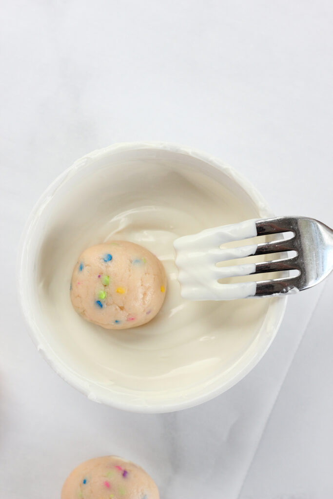 top down shot showing melted white chocolate in a small white bowl. A truffie is sitting inside with a fork 