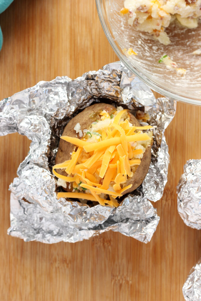 Top down shot showing a baked potato in a foil wrapping topped with a heaping amount of shredded cheese