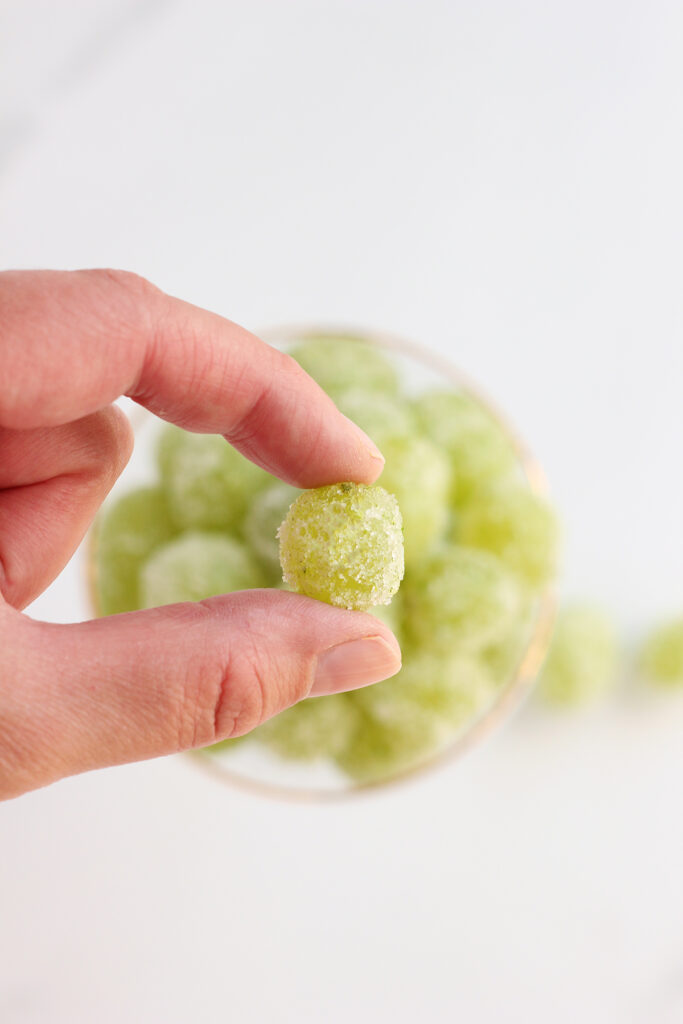 hand holding a sugar coated green grape over a stack of other grapes