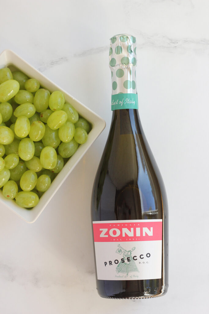 top down image showing a square colander filled with green grapes and a bottle of Zonin Prosecco 