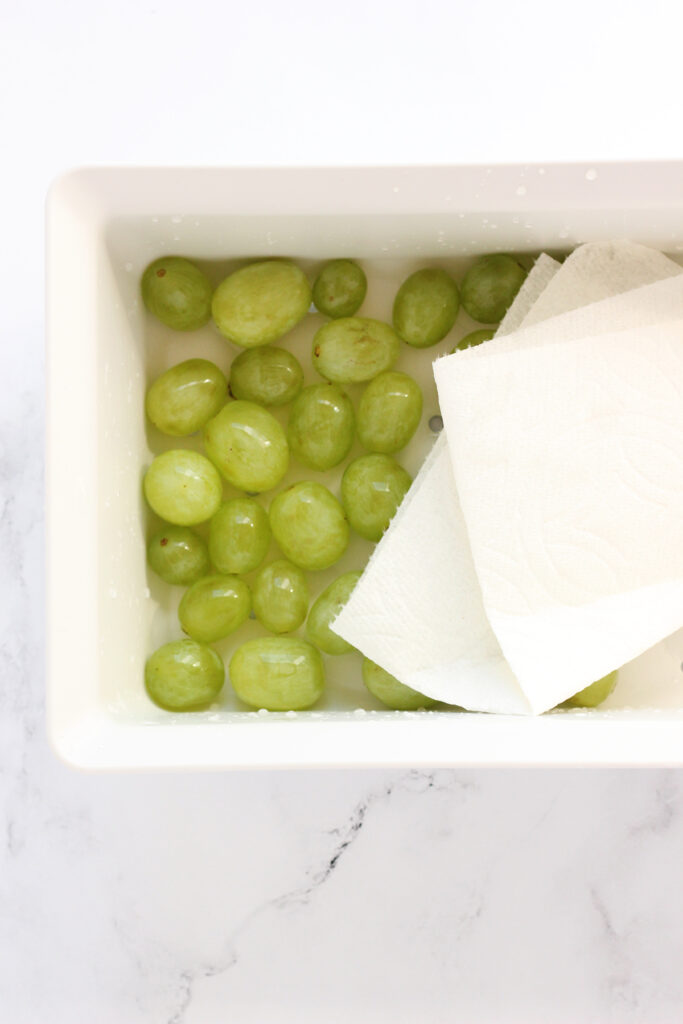 top down image showing a white rectangle colander filled with clean crapes and a napkin. The colander is sitting on a white marble counter. 